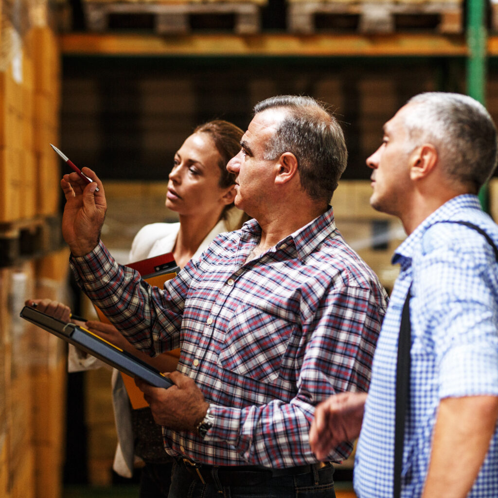 Team of customs managers and warehouse worker checking list and inventory on the shelf in storehouse.