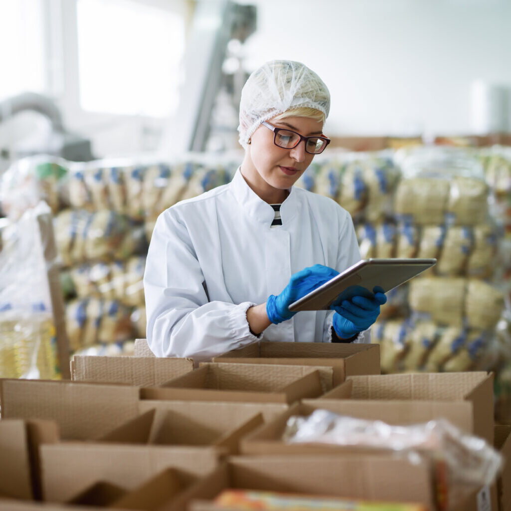 Female worker using tablet for checking boxes while standing in food factory.